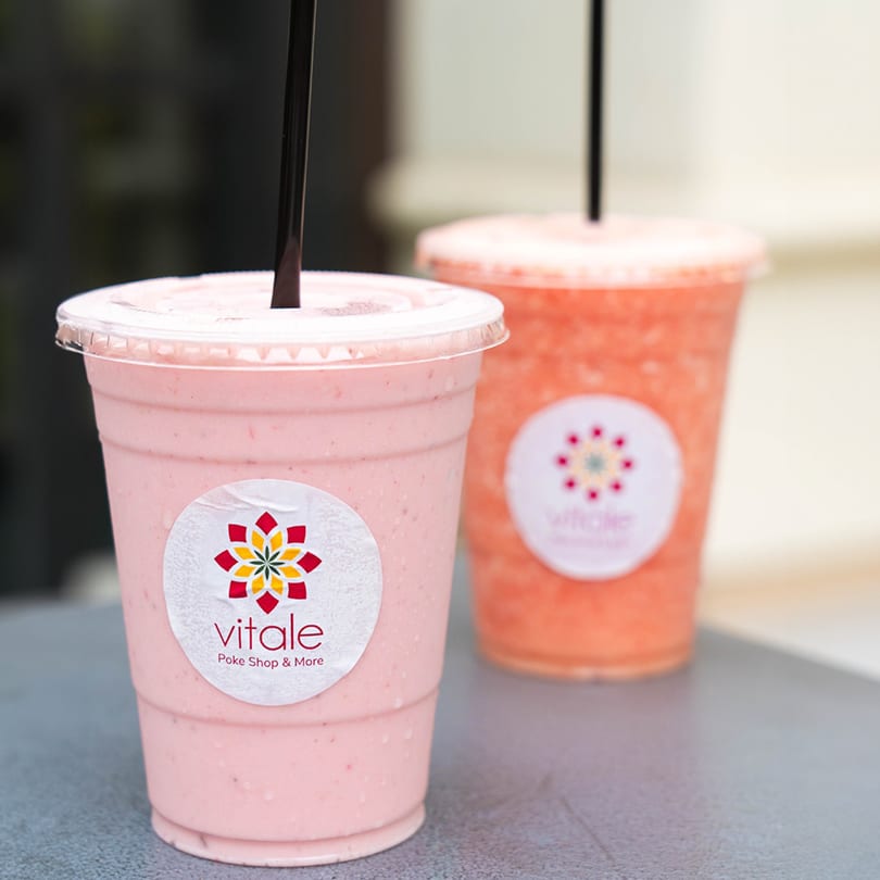 Two Vitale Poke Shop & More smoothies, one pink and one orange, with black straws.