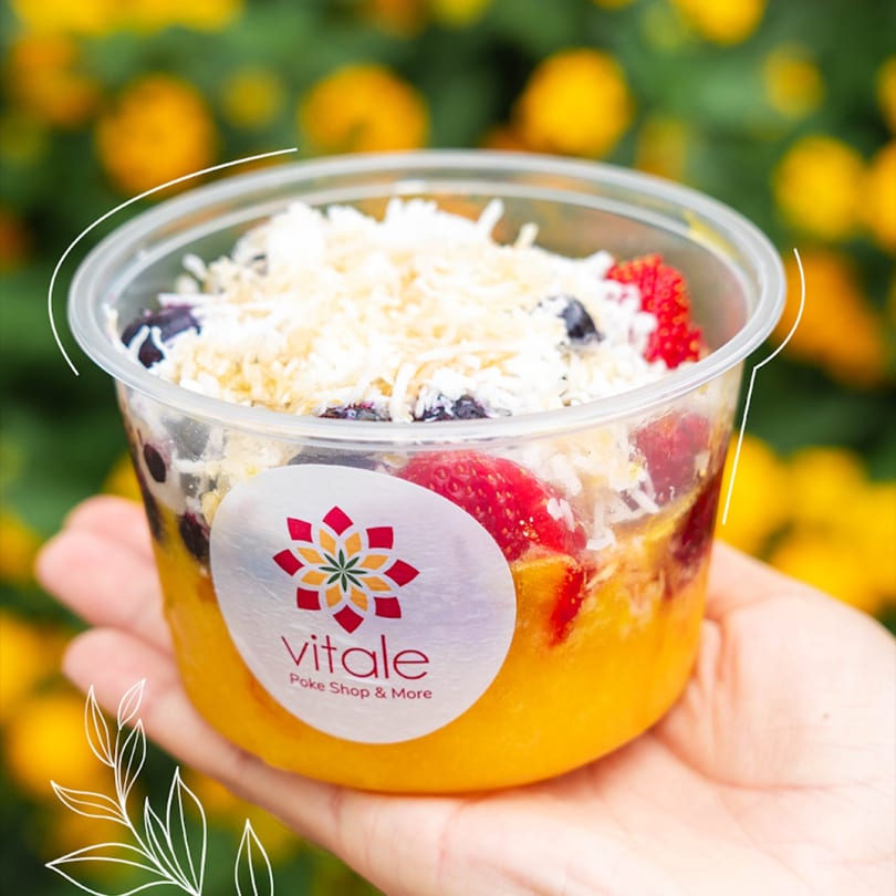 A hand holds a clear plastic cup of Vitale Poke Shop & More fruit bowl with berries and coconut.